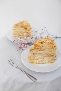 Beyaz arka planda izole edilmiş beyaz bir fincan tabağında Napolyon pastası. Ekşi kremalı puf böreği. Boşluğu kopyala.