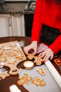 Kırmızı kazaklı bir kız zencefilli kurabiye süslüyor. Onları mutfakta şekerle süsledi. Noel evi konsepti.