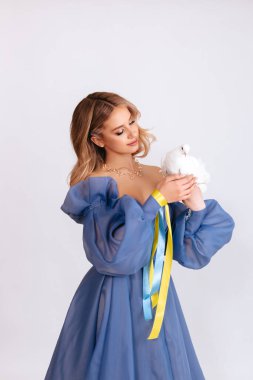 Ukrayna için dua et. Mavi kabarık elbiseli, Ukrayna bayrağı renginde kurdeleli genç bir kadın beyaz arka planda barışın beyaz güvercin sembolünü taşıyor. Savaşı durdurun. Boşluğu kopyala.