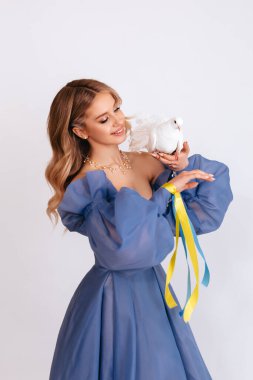 Ukrayna için dua et. Mavi kabarık elbiseli, Ukrayna bayrağı renginde kurdeleli genç bir kadın beyaz arka planda barışın beyaz güvercin sembolünü taşıyor. Savaşı durdurun. Boşluğu kopyala.