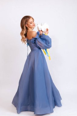 Ukrayna için dua et. Mavi kabarık elbiseli, Ukrayna bayrağı renginde kurdeleli genç bir kadın beyaz arka planda barışın beyaz güvercin sembolünü taşıyor. Savaşı durdurun. Boşluğu kopyala.