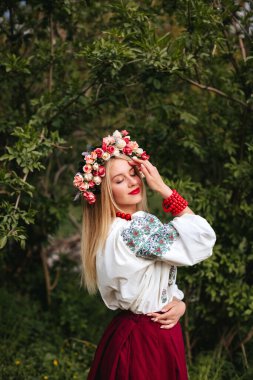 Ukrainian woman in a traditional Ukrainian dress and with a wreath of flowers on her head poses with her eyes closed in nature. 