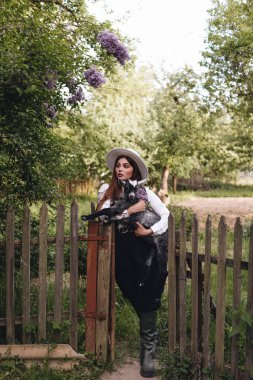 Beyaz bluzlu, siyah yelekli, beyaz şapkalı güzel bir kız köyde küçük bir keçiyi elinde tutuyor. Kırsal yaşam.