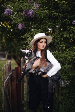 Mutlu bir çiftçi kızı küçük siyah beyaz bir keçiye sarılır. Kırsal yaşam.