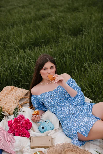 Piękna Dziewczyna Długimi Włosami Niebieskiej Sukience Zjada Rogalika Pikniku Przyrodzie — Zdjęcie stockowe