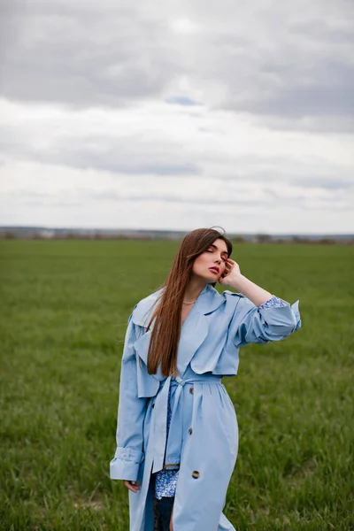 Stylowa Dziewczyna Długimi Ciemnymi Włosami Pozująca Niebieskim Płaszczu Zielonym Polu — Zdjęcie stockowe