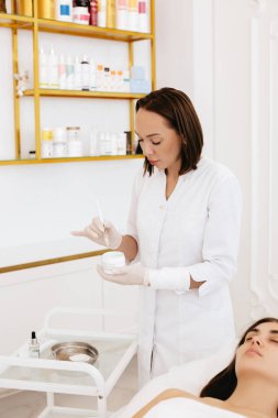 The cosmetologist holds in his hands a cream with a brush for application in a beauty salon.