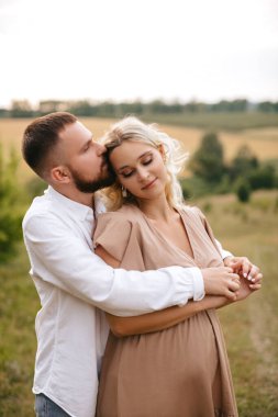 Loving man hugging his pregnant wife from behind in nature. Autumn love. 