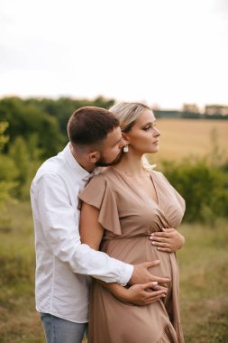 Loving man hugging his pregnant wife from behind in nature.
