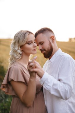 Young couple hugging and holding hands in nature. A man with his pregnant wife show their feelings.