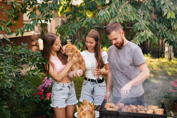 Family barbecue grill in the garden. Barbecue party. A family with a ginger cat is having fun and chatting on the grill.
