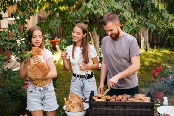 Family barbecue grill in the garden. Barbecue party. A family with a ginger cat is having fun and chatting on the grill.