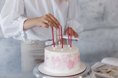 Kremalı pastayı gri arka planda pembe mumlarla süsleme süreci..