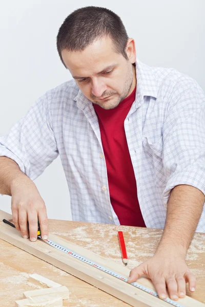 Holzarbeiten - Mann misst Holzplanke — Stockfoto