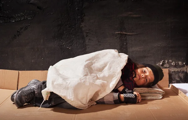 Niño mendigo durmiendo en la hoja de cartón — Foto de Stock