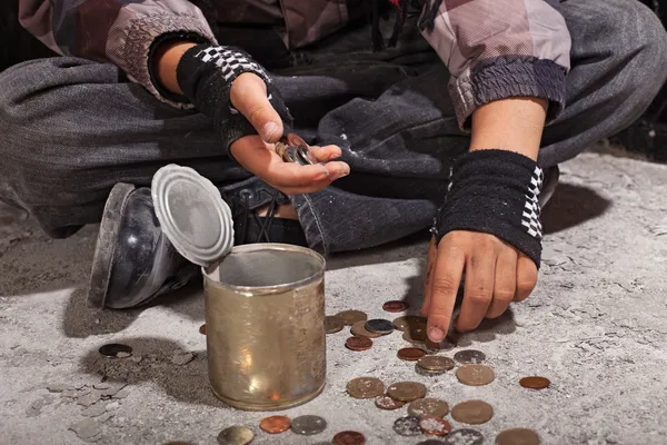 Нищий ребенок считает монеты, сидя на поврежденном бетонном полу — стоковое фото