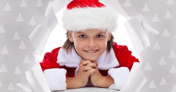 Buon Natale ragazzo sorridente attraverso il buco in carta da imballaggio — Foto Stock