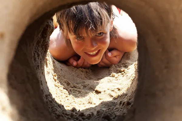 Happy boy na pláži pohledu tunelem pod hrad z písku — Stock fotografie