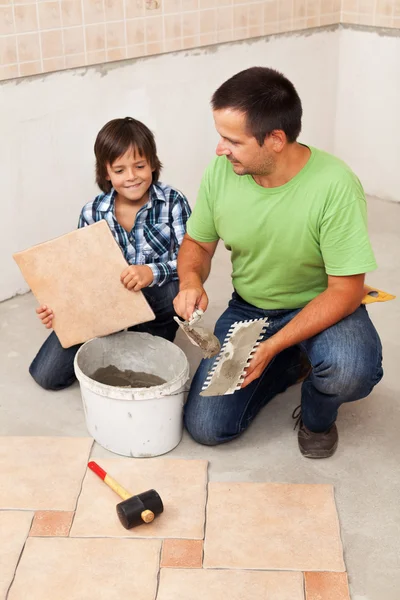 Man laying ceramic floor tiles helped by small boy — Stock Photo, Image