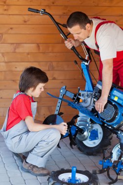Boy helps his father mounting a cultivator machine clipart