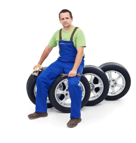 Vriendelijke auto-mechanic zittend op banden — Stockfoto