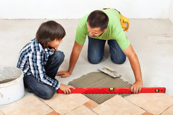 Man and boy laying ceramic floor tiles together — Stock Photo, Image