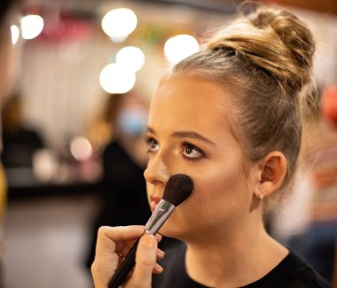 Makyöz, kozmetik ürününü genç kızın yanağına fırçayla sür - yüzüne yakın çekim