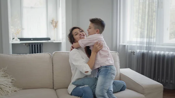 Nuori äiti ja poika sohvalla. Äiti halaa poikaa. Heillä on hauskaa.. — kuvapankkivalokuva