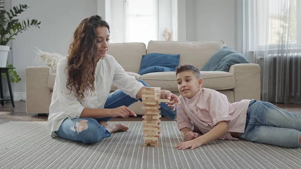 Mutter und Sohn sitzen auf dem Fußboden in der Wohnung. Sie spielen das Spiel der Montage der Pyramide aus Holzstäben. Stockbild