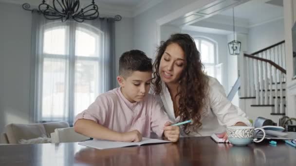 Jovem mãe e filho à mesa. Boy Writes In Notebook. Ele faz seu dever de casa. — Vídeo de Stock