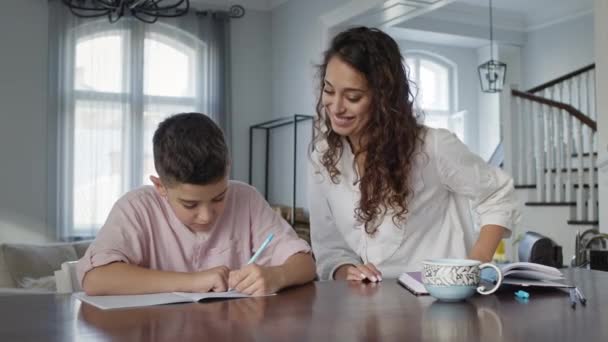 Jeune mère et son fils à la table. Boy écrit dans un carnet. Il fait ses devoirs. — Video