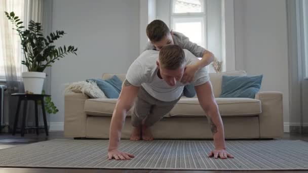 Mladý otec vymačkává z podlahy svého syna na zádech. — Stock video