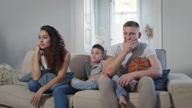 Odadaki koltukta oturan genç bir aile. Televizyon izleyip spor oyunları için tezahürat yapıyorlar..