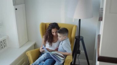 Genç anne ve oğlu birlikte kitap okuyor. Uzun kıvırcık saçlı, elinde kitap tutan genç ve güzel bir kadın..