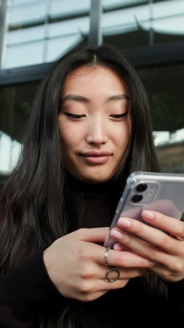 Porträt eines koreanischen Mädchens mit dem Handy in der Hand. Mädchen blickt auf den Telefonbildschirm. Nahaufnahme. — Stockvideo
