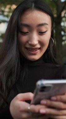 Elinde cep telefonuyla sokakta oturan Koreli kız. Kız telefon ekranına bakıyor. Kapat..