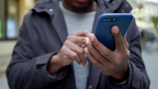 Hände des schwarzen Mannes. Er hält das Telefon in der Hand und fährt mit dem Finger aktiv über den Bildschirm. — Stockvideo