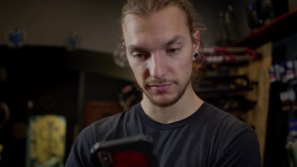 Jeune homme avec téléphone dans les mains debout dans l'atelier de vélo. Il utilise activement le téléphone. — Video