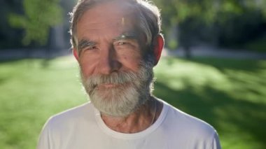 Sakallı, gri saçlı adamın yüzü. O, parkta. Güneş ışınları onu aydınlatır. Gülümsüyor..