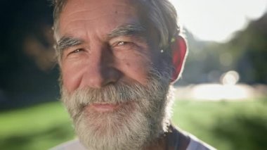 Sakallı, gri saçlı adamın yüzü. O, parkta. Güneş ışınları onu aydınlatır. Gülümsüyor..