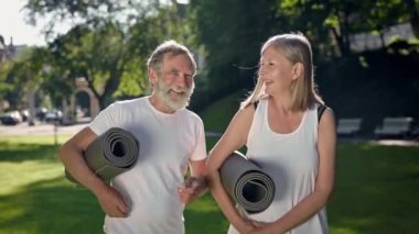 Parkta ellerinde spor minderleriyle yürüyen iki yaşlı insan. Güzel konuşuyorlar. Gri saçlı sakallı adam ve uzun saçlı kadın. Park 'ta Sabah Sporu. Güneşli Yaz Günü.