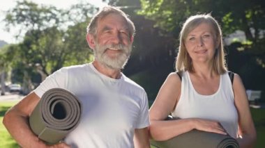 Parkta ellerinde spor minderleriyle bekleyen iki yaşlı insan. Güzel konuşuyorlar. Gri saçlı sakallı adam ve uzun saçlı kadın. Park 'ta Sabah Sporu. Güneşli Yaz Günü.