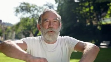 Yaşlı adam parka spor yapmaya gider. Zıplar ve mutlu bir şekilde bağırır. Sakallı Gri Adam. Yaz Güneşli Günü.