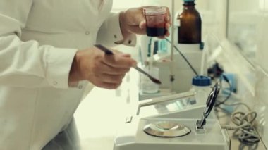 Ölçüm cihazına sıvı damlatan laboratuvar teknisyeni. Kadın, şeker sayacının kapağını kapattı. Siyah sıvı bir şişenin içinde. Beyaz bornoz giyen kadın..