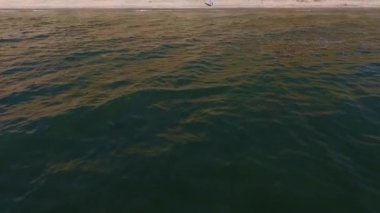 Sıcak bir plajda yürüyen genç bir kadın. Kız Suya Gidiyor. Denizin Fırtınalı Dalgaları. Model üzerinde uzun, açık, bedava bir elbise var.