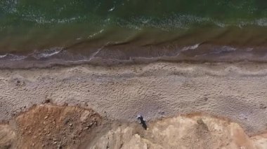 Hava görüntüsü. Sıcak bir plajda yürüyen genç bir kadın. Kızın gölgesi kumun üzerine düşüyor. Denizin Sakin Dalgaları. Model üzerinde uzun, açık, bedava bir elbise var.
