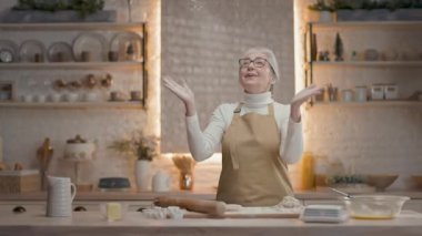 Mutfaktaki Kadın Hazırlık. Yeni yıl tatiline hazırlanıyor. Kadın eğleniyor. Unu havaya fırlatıyor. Masa Hamuru 'nda. Gri saçlı sevimli büyükanne..