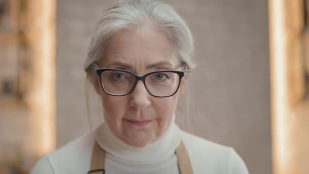 四月中女人的画像 她站在厨房里 戴眼镜头发灰白的漂亮女人 她身后有许多带着工具的架子 她笑了 — 图库视频影像