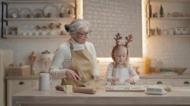 Noel tatilleri. Büyükannem ve küçük kızım mutfakta. Arkalarında teçhizatlı bir sürü raf var. Kız, farklı şekillerde hamur şekline bürünüyor. Büyükanne Yumurta Döver. Noel yapıyorlar.