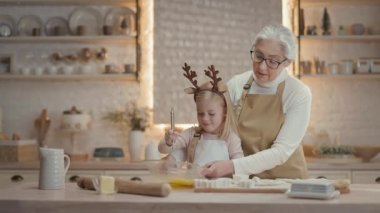 Büyükannem ve küçük kızım mutfakta. Arkalarında bir sürü alet edevat rafı var. Büyükannem, kıza yumurta çırpmayı öğretiyor. Tabağı tutuyor ve çocuğa yardım ediyor. Büyükanne Çocuğa Sarıldı.
